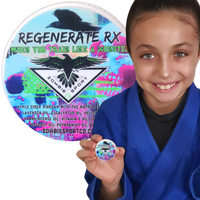 A smiling girl, numerous time jiu jitsu gold medalist, in a blue martial arts uniform holds a small, round branded medallion in front of a large matching circular graphic. The medallion and graphic feature a black raven, the text 'REGENERATE RX' and 'ZOMBIE SPORT', and a colorful abstract background.